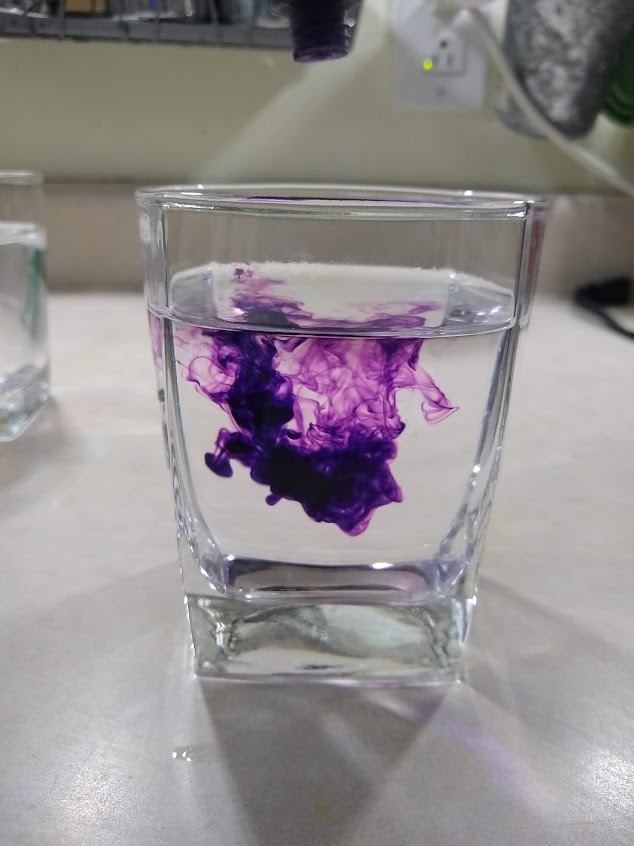 Image of purple food dye in hot water, food dye in a cloud in the center of the glass.